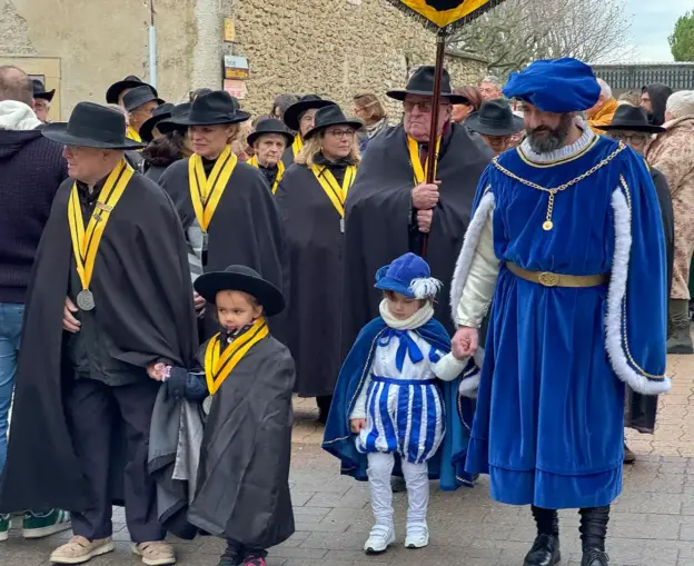Menschen in mittelalterlichen Kostümen, darunter auch Kinder, stehen im Freien zusammen; einige tragen Orden und schwarze Umhänge.