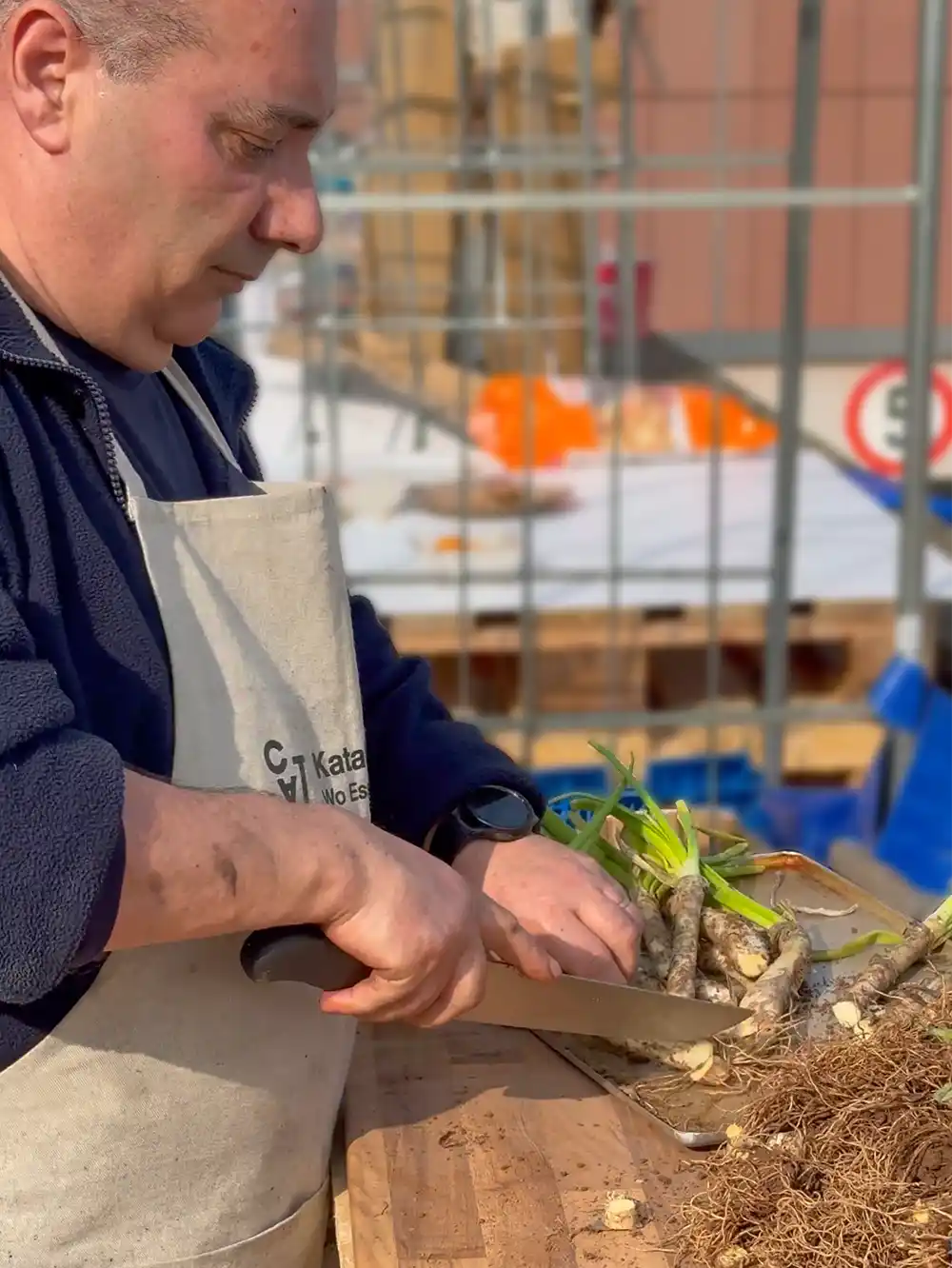 Eine Person schneidet frische Frühlingszwiebeln mit einem Messer auf einer Holzunterlage im Freien.