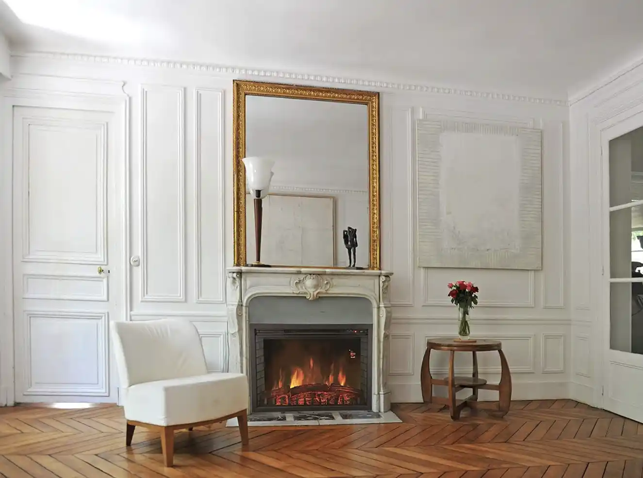 Elegantes Wohnzimmer mit einem weißen Sessel, einem Kamin, einem großen Spiegel, einem Beistelltisch und einer Blumenvase.