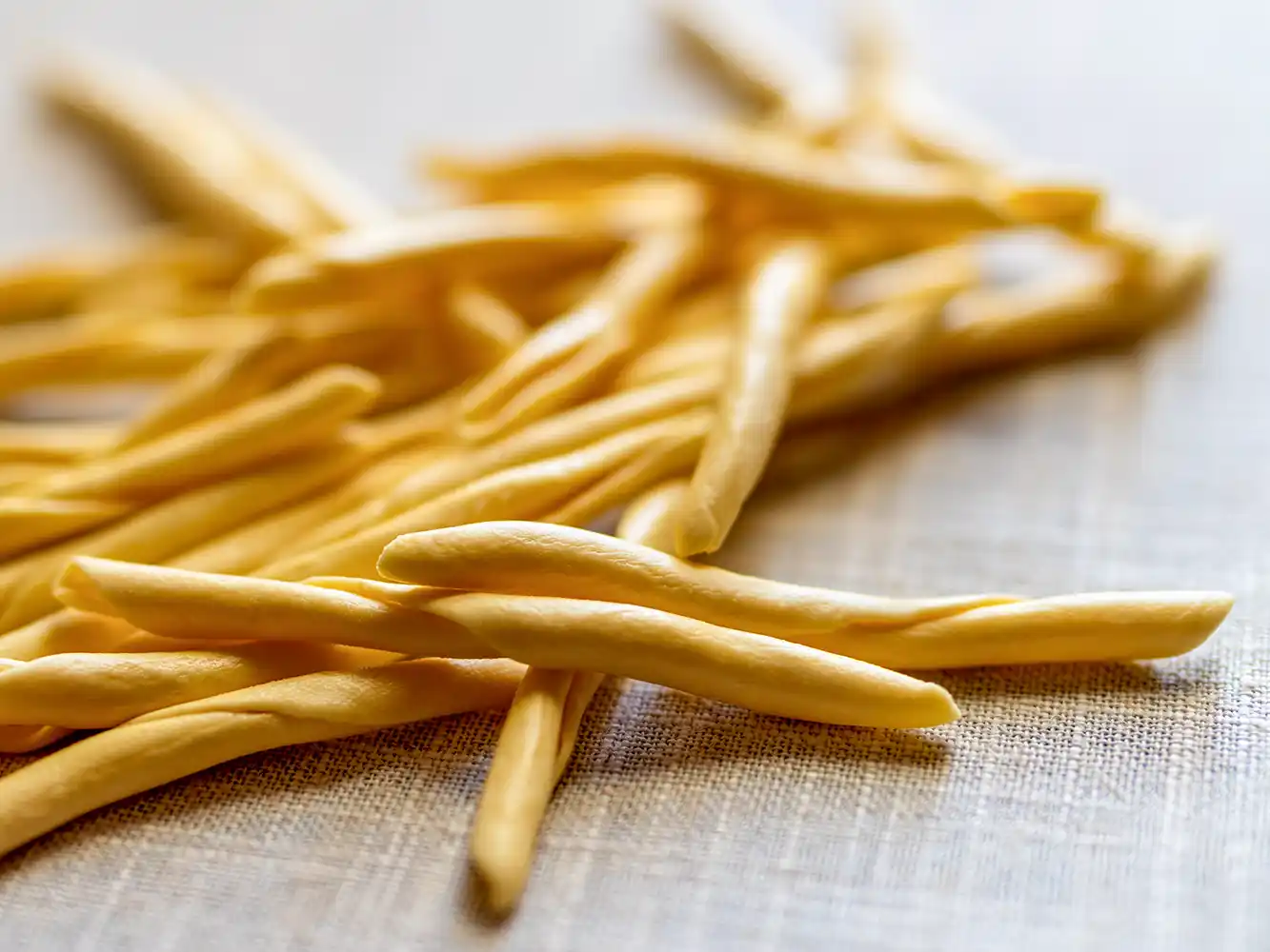 Ein Haufen ungekochter, gedrehter Nudeln liegt auf einer leichten Stoffoberfläche.