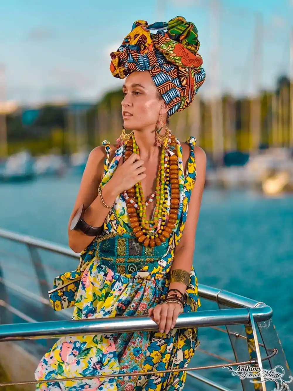 Eine Frau in farbenfroher traditioneller Kleidung und Kopfbedeckung steht am Wasser und trägt mehrlagige Perlenketten.