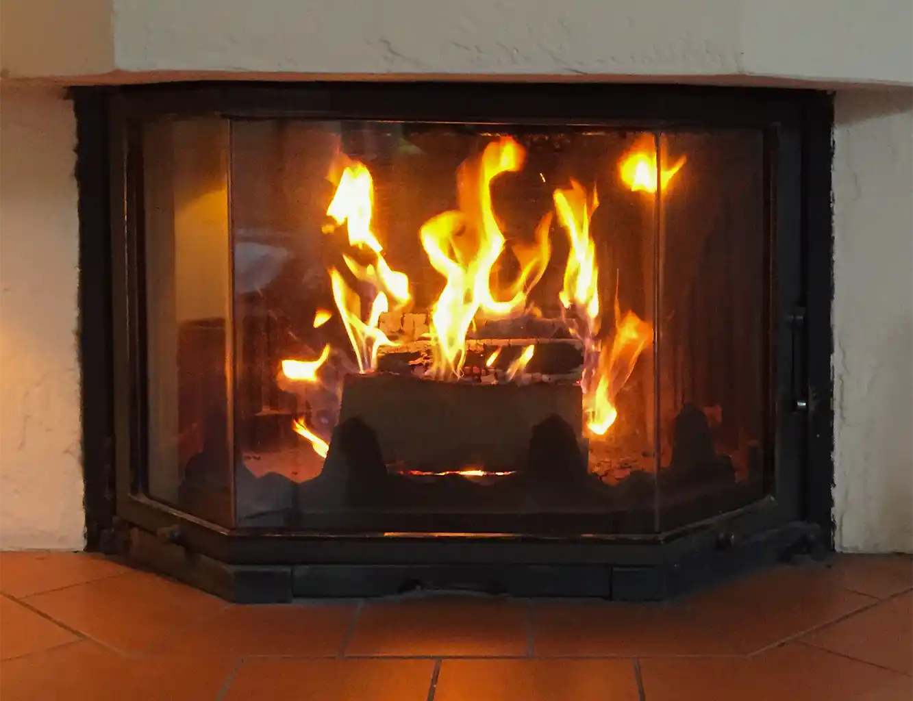 Ein helles Feuer brennt in einem verglasten Kamin auf einer gekachelten Feuerstelle.