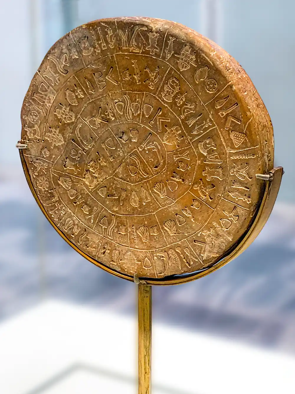 Runde Tonscheibe mit spiralförmiger antiken Schriftzeichen, aufrecht stehend auf einem Metallständer in einer Museumsumgebung.