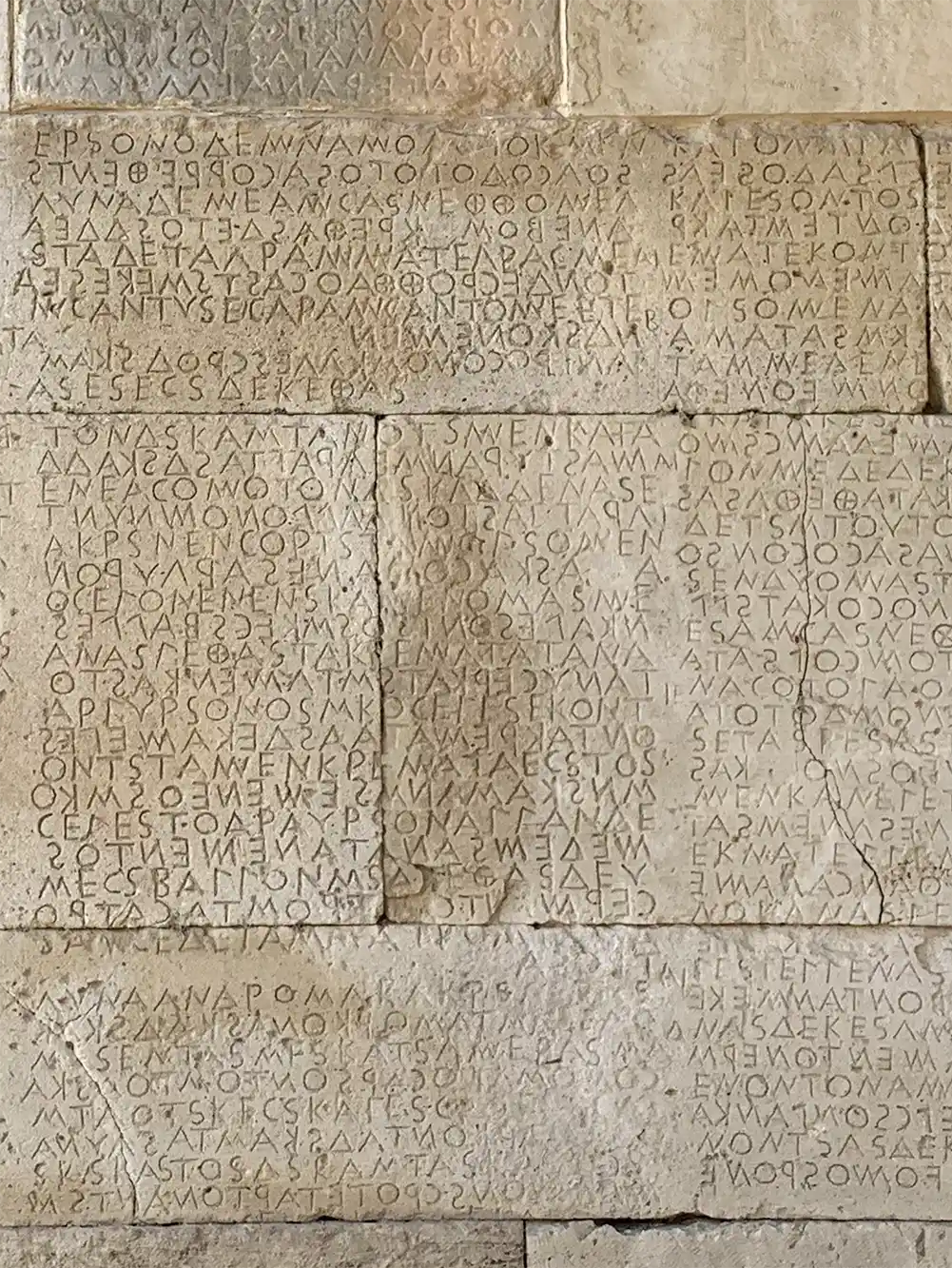 Antike Steinmauer mit griechischen Inschriften in ordentlichen, gleichmäßigen Reihen eingemeißelt.