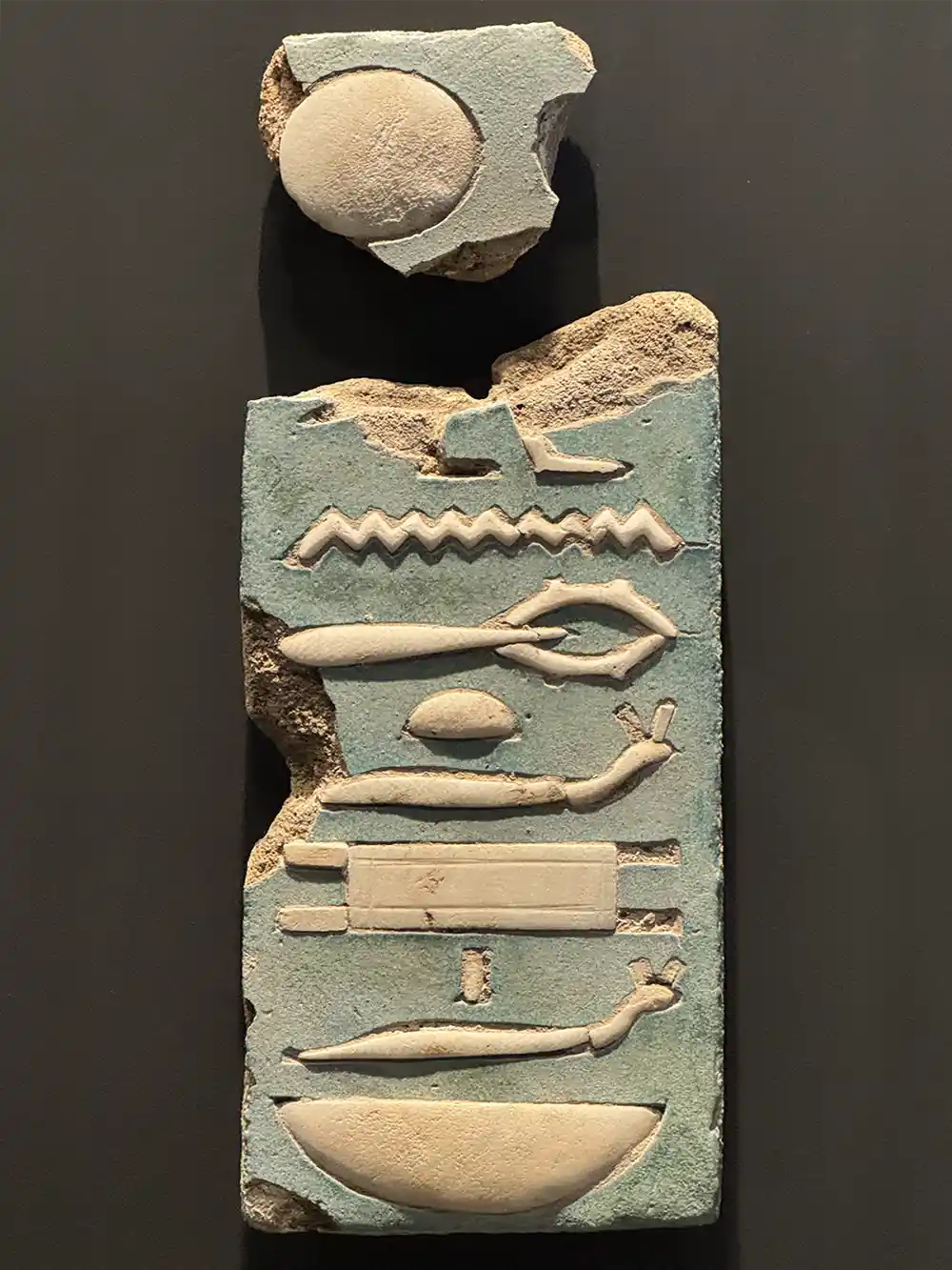 Altägyptisches Hieroglyphenrelief auf einer zerbrochenen Steinplatte mit blauen und weißen Schnitzereien.