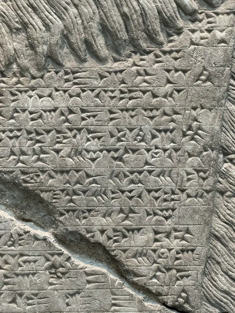 Antike Steintafel mit reihenweise eingemeißelter Keilschrift, die einige Risse und Verwitterungen aufweist.