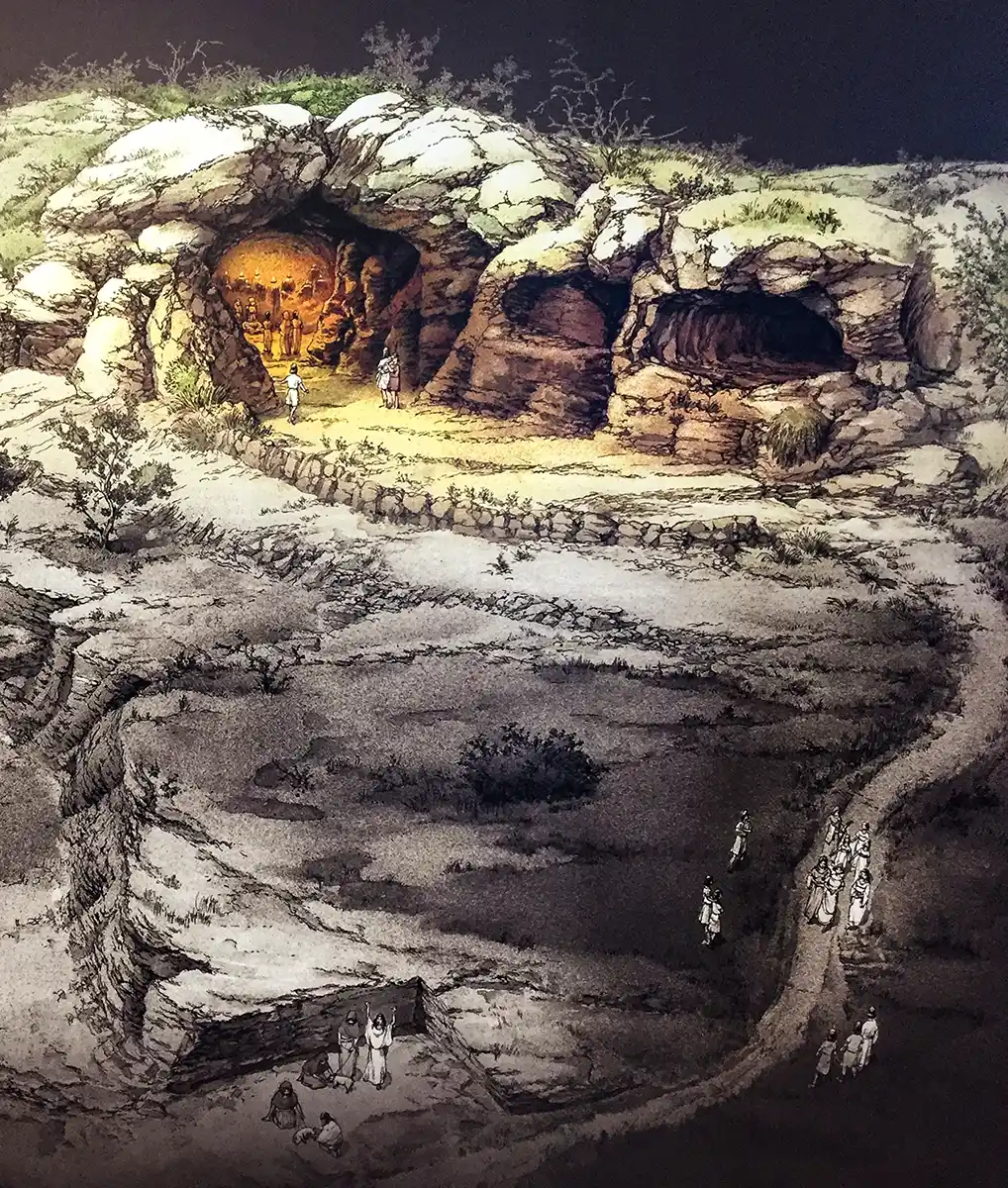 Eine Gruppe von Menschen nähert sich beleuchteten Höhlen, die in einen felsigen Abhang gehauen sind und zu deren Eingang Wege führen.