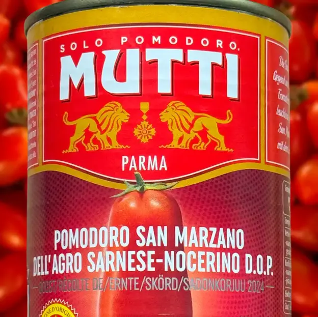 Eine Mutti-Dose mit San Marzano-Tomaten mit rotem Etikett und goldenen Löwen, umgeben von frischen Tomaten.