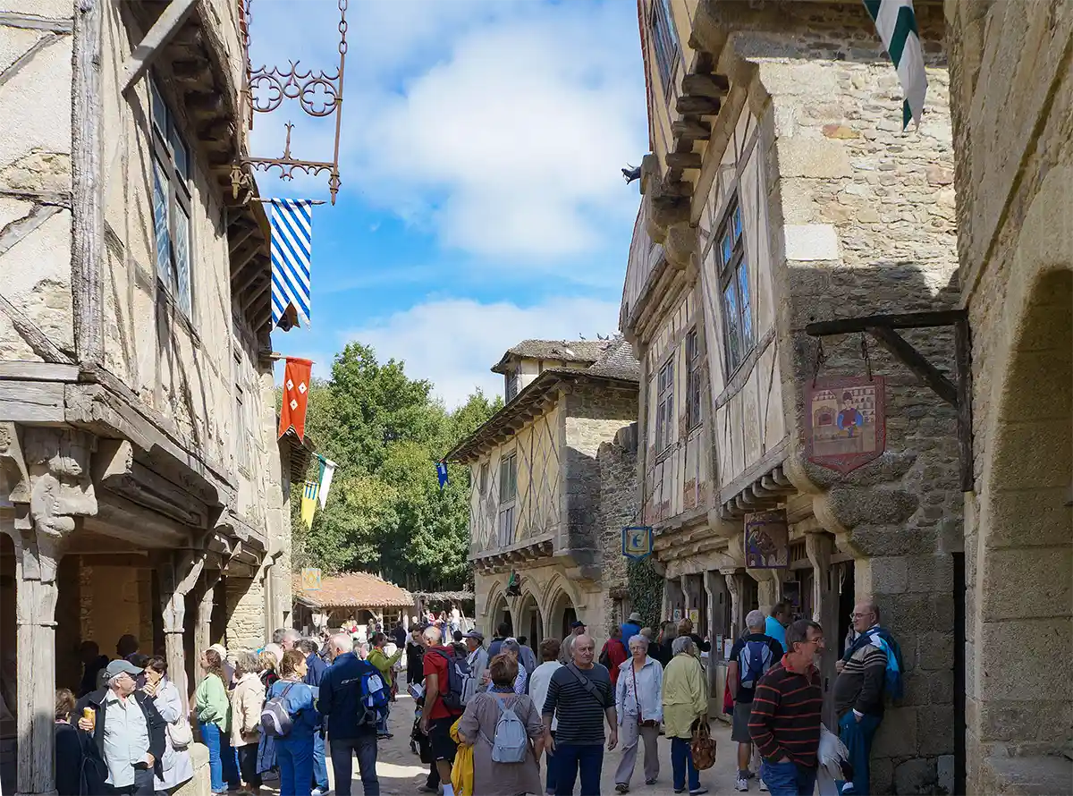 Menschen auf einer schmalen Straße, die von alten Steinhäusern und bunten Fahnen gesäumt ist.
