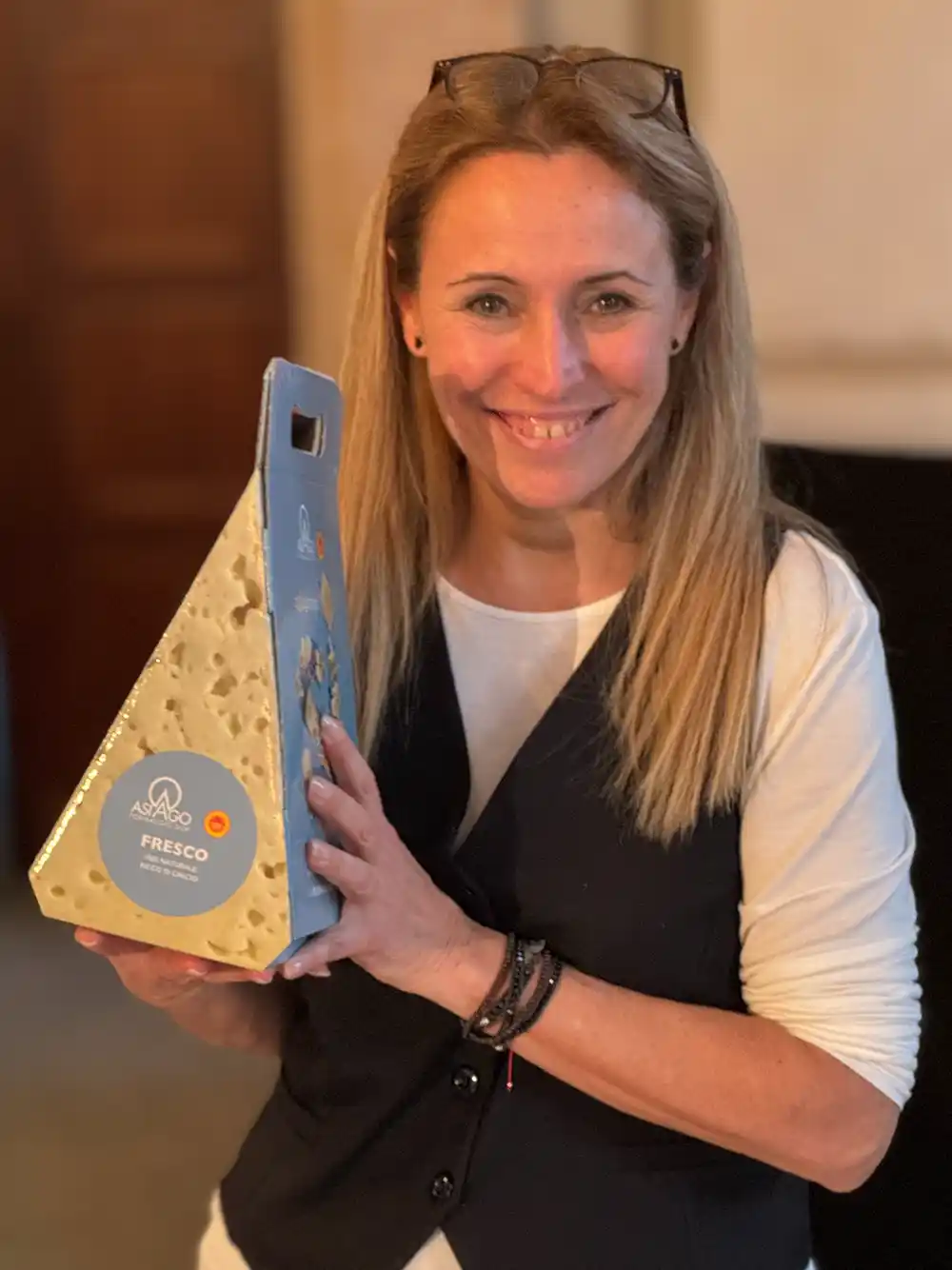 Frau lächelt und hält ein großes Stück Asparago Fresco-Käse mit hellblauem Etikett.