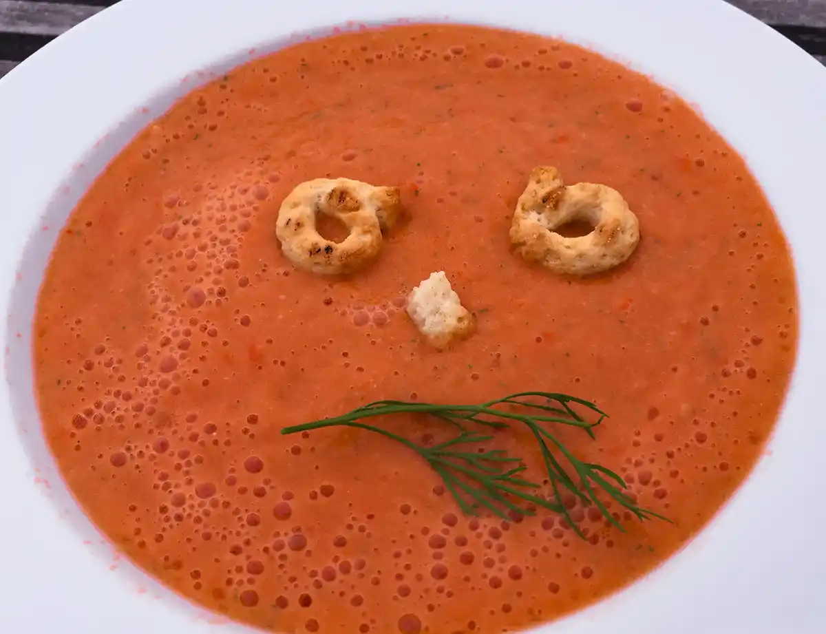 Eine Schüssel Tomatensuppe mit Crackern und Kräutern, die so angeordnet sind, dass sie wie ein trauriges Gesicht aussehen.