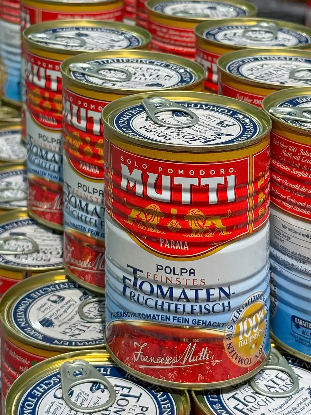 Dosen mit fein gehackten Mutti-Tomaten, die dicht an dicht in einem Regal stehen.