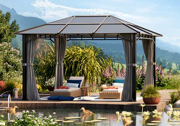 Ein Pavillon mit Liegestühlen an einem Teich, umgeben von üppigem Grün und Blumen an einem sonnigen Tag.