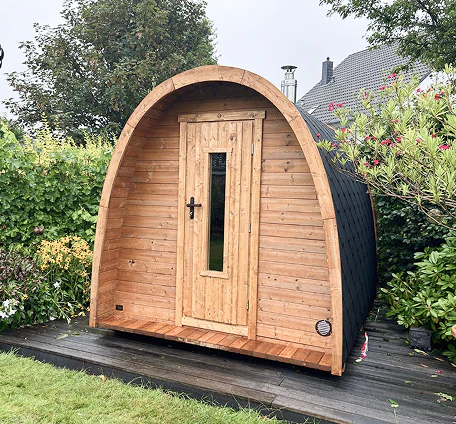 Eine kleine, gewölbte Holzhütte mit einer zentralen Tür, die auf einem Holzdeck in einem Garten steht.