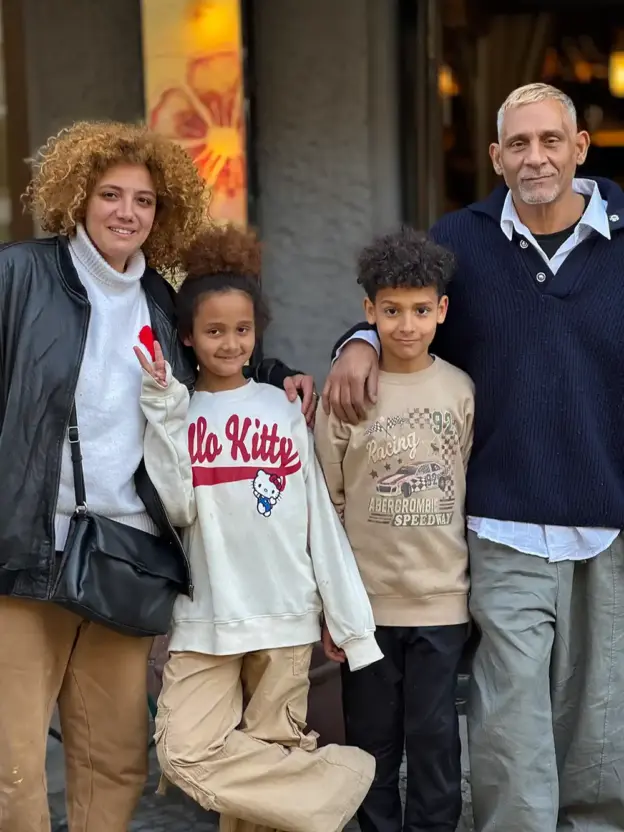 Eine lächelnde vierköpfige Familie posiert gemeinsam im Freien, zwei Erwachsene und zwei Kinder, wobei ein Kind ein Friedenszeichen macht.