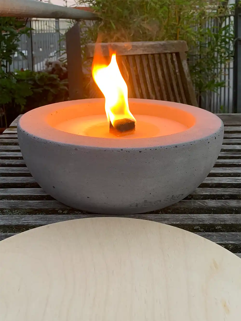 Feuer-Balkon-Betonschale-Holzdeckel Eine Tischfeuerschale aus Beton, davor ein runder Holzdeckel