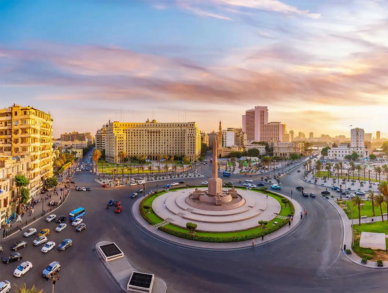 Der Tahrir-Platz in Kairo, Ägypten, mit Verkehr, Gebäuden und einem zentralen Obelisken bei Sonnenuntergang.