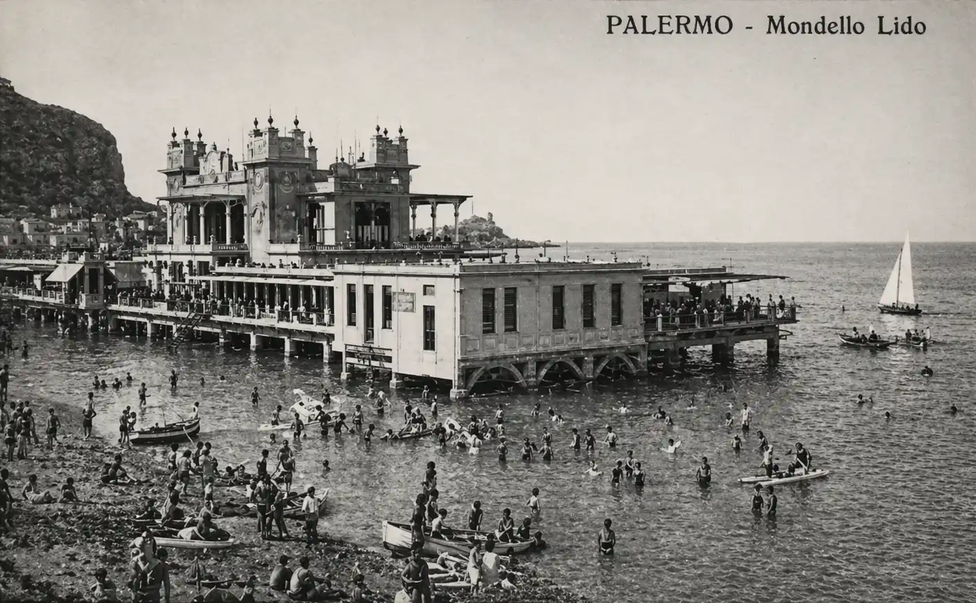 Vintage-Foto von Palermos Mondello Lido mit schwimmenden Menschen und einem Gebäude auf Stelzen über dem Wasser.