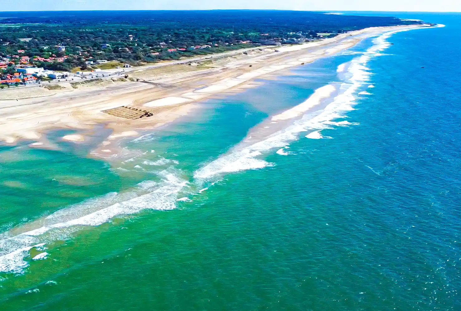 Atlantik-Strand-Soulac-2 Luftaufnahme eines langen Sandstrands mit Wellen und türkisfarbenem Wasser, der sich entlang der Küstenlinie erstreckt.