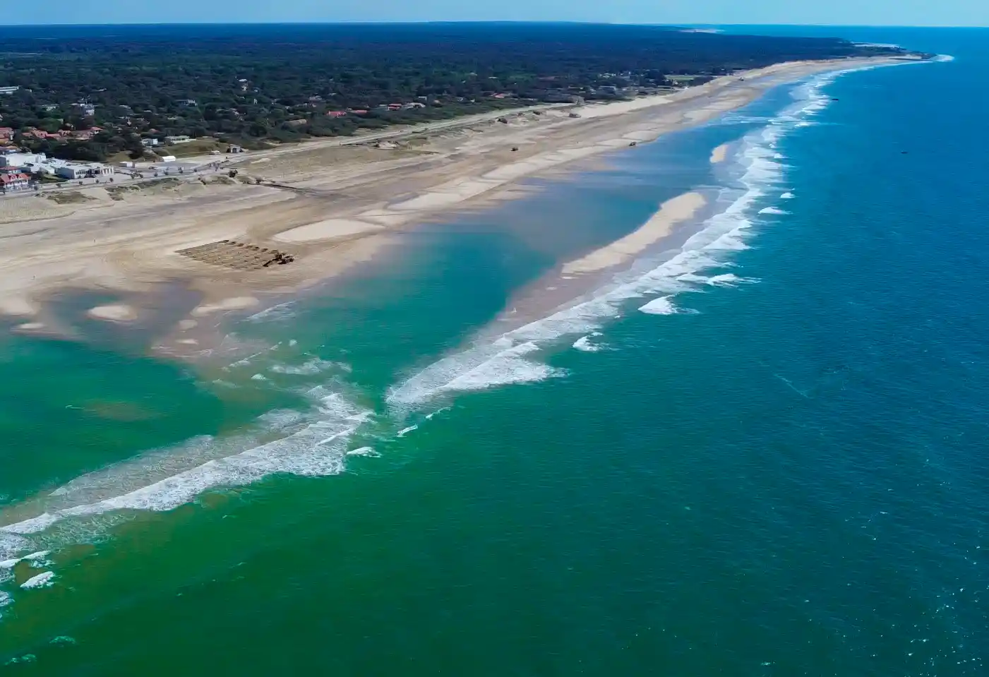 Atlantik-Strand-Soulac Luftaufnahme eines langen Sandstrands mit Wellen und türkisfarbenem Wasser, der sich entlang der Küstenlinie erstreckt.