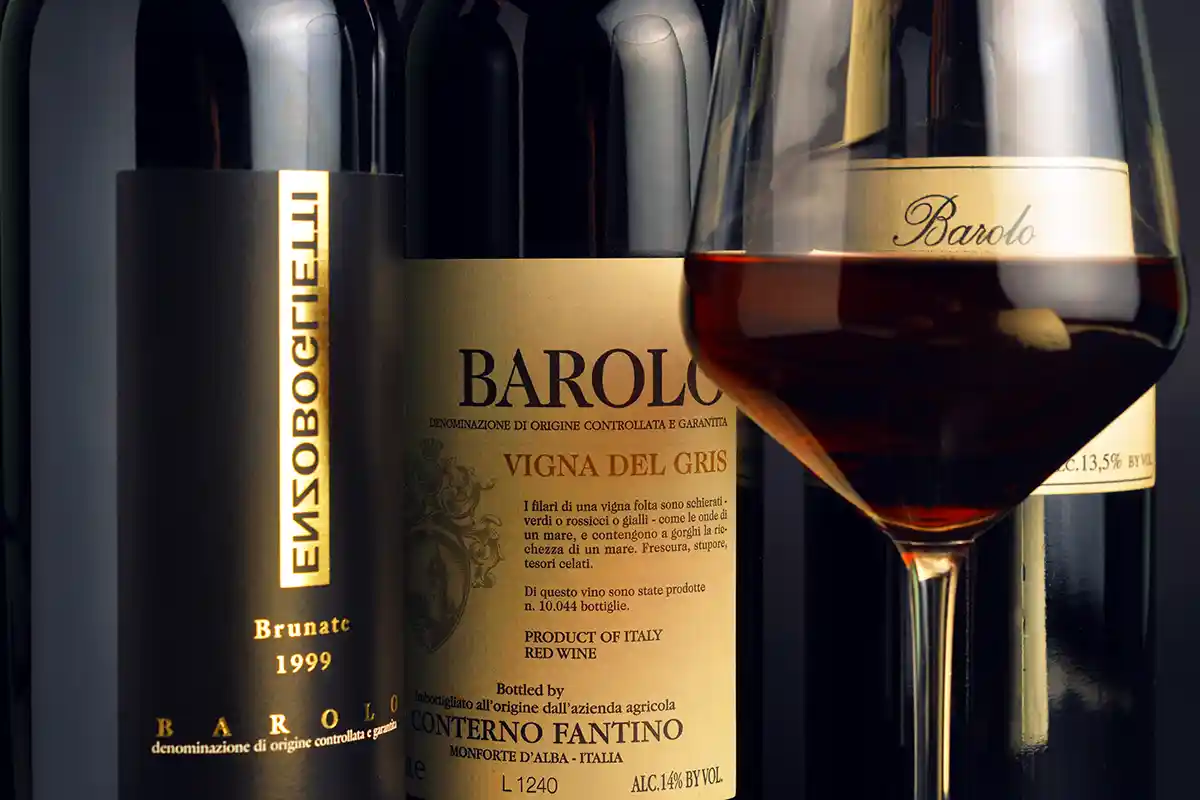 Barolo-Wein Drei Flaschen Barolo-Rotwein und ein gefülltes Weinglas, Etiketten sichtbar, mit eleganter Beleuchtung.