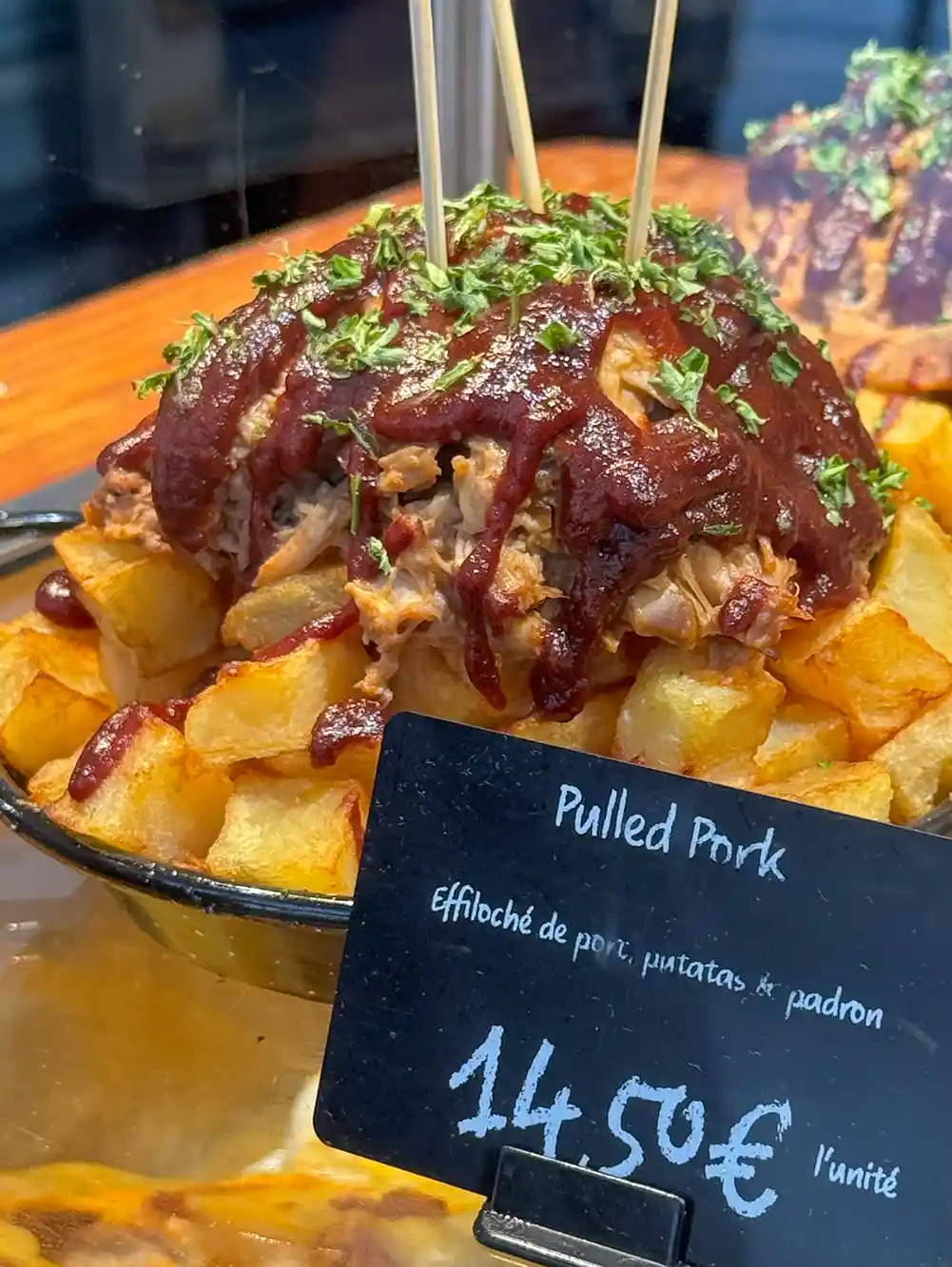 Eine Schüssel Pulled Pork mit Barbecue-Soße auf knusprigen Kartoffeln, garniert mit Kräutern, mit einem Preisschild davor.