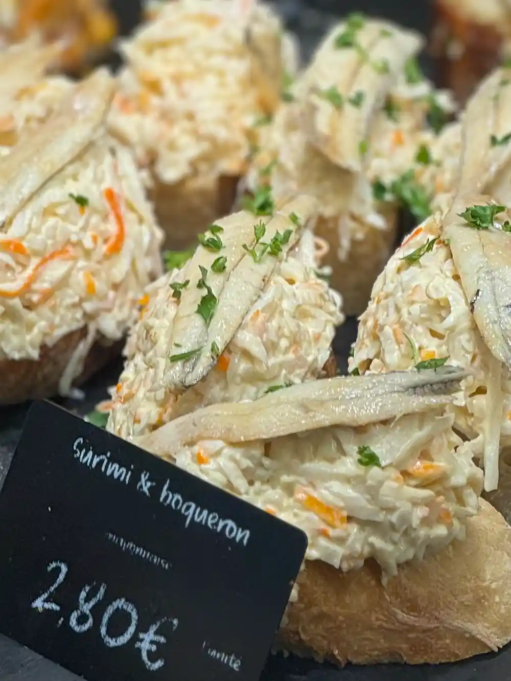 Brotscheiben, belegt mit Surimi-Salat, marinierten Sardellen und gehackter Petersilie, zum Preis von 2,80 €.
