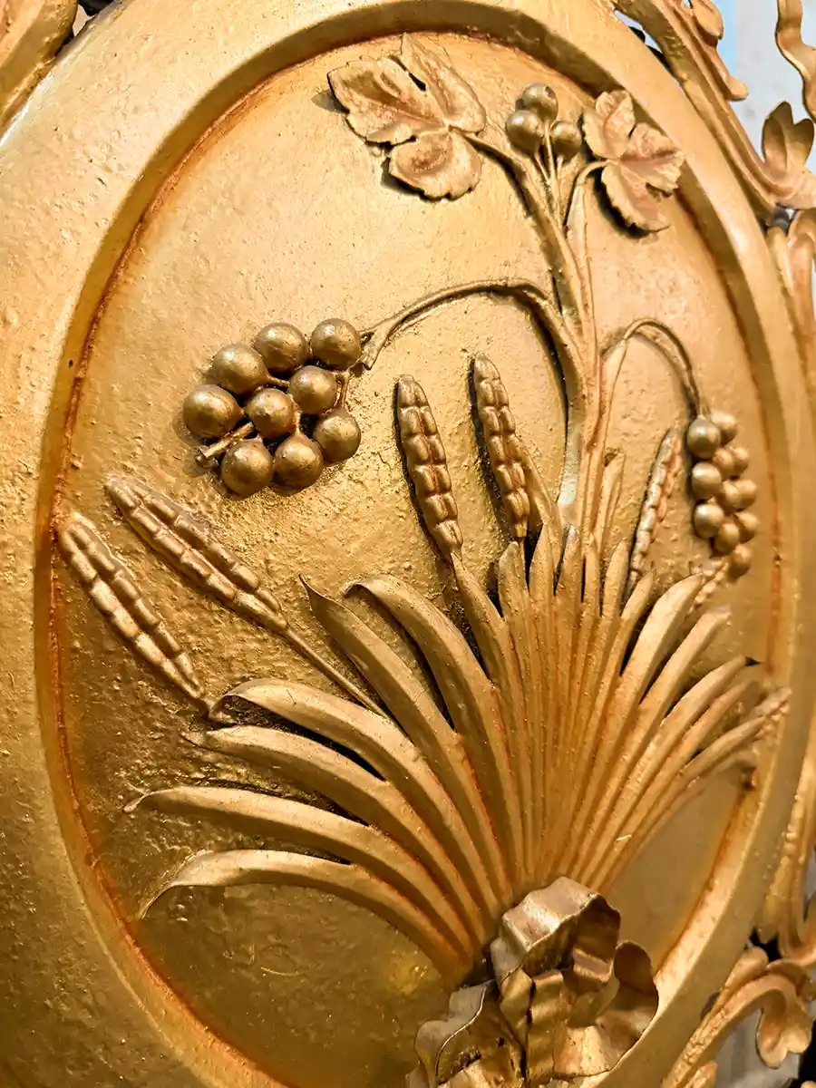 Bordeaux-Geheimtipps-Notre-Dame-de-Bordeaux-Goldarbeiten Goldgeprägtes Design aus Weizen und Beeren auf einer ovalen Plakette mit Blattdetails.