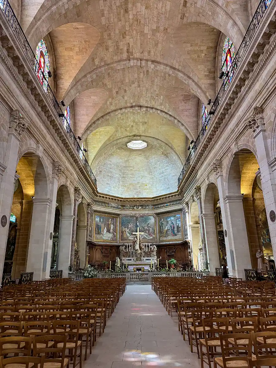 Bordeaux-Geheimtipps-Notre-Dame-de-Bordeaux-innen Das Innere einer großen Steinkirche mit gewölbten Decken, bunten Glasfenstern und Reihen von Holzstühlen.
