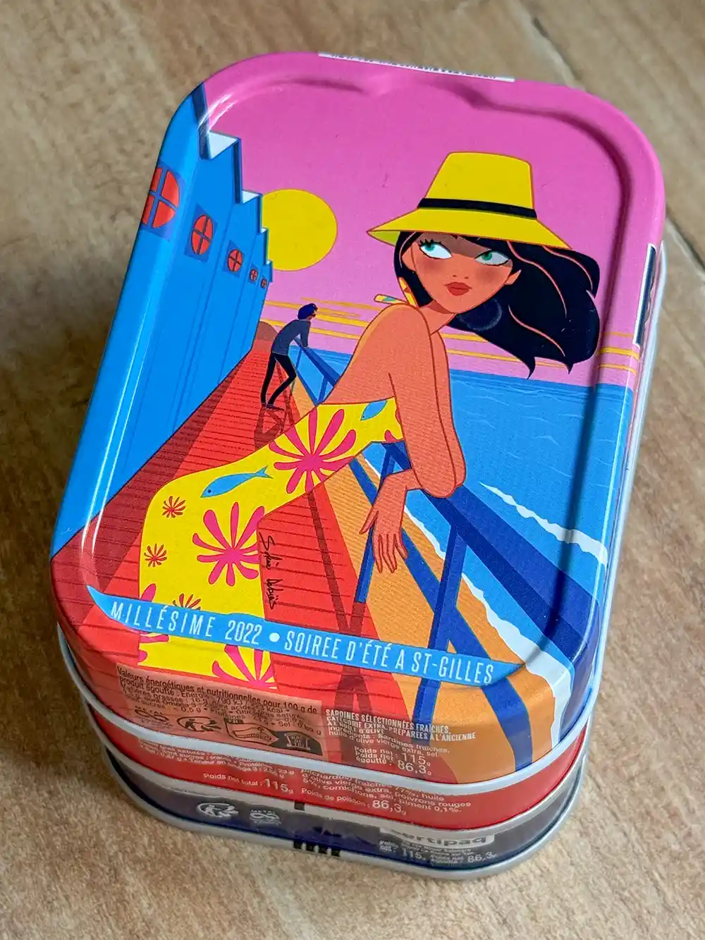 Bunte Dose mit einer Illustration im Retrostil einer Frau mit gelbem Hut auf einer Strandpromenade bei Sonnenuntergang.