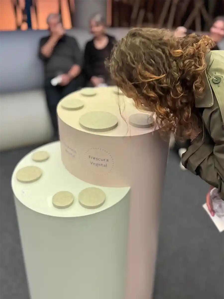 Bordeaux-Geheimtipps-Via-Sensoria-Duefte Eine Person riecht an einem Ausstellungsstück, während andere im Hintergrund sitzen und zusehen.