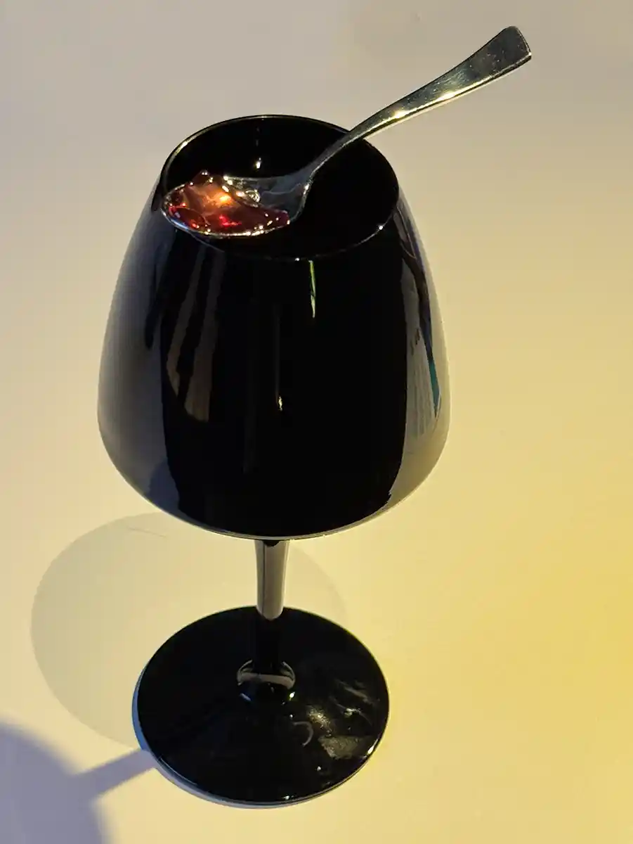 Bordeaux-Geheimtipps-Via-Sensoria-Glas Ein schwarzes Weinglas mit einem Löffel darin, der eine rote, geleeartige Substanz enthält.