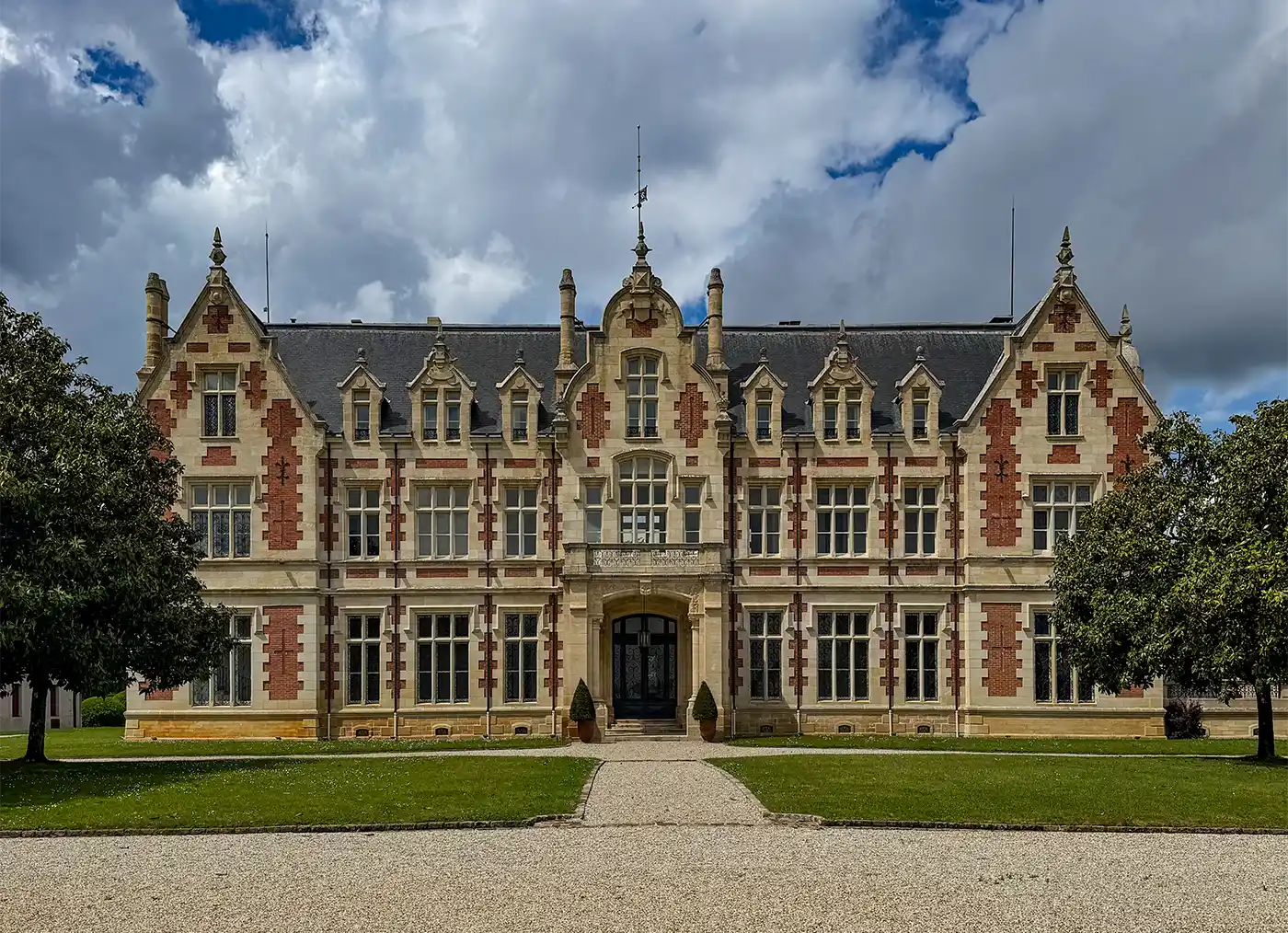 Ein prächtiges historisches Gebäude mit verschnörkelter Architektur, roten Backsteinakzenten und einem zentralen Bogeneingang unter einem bewölkten Himmel.