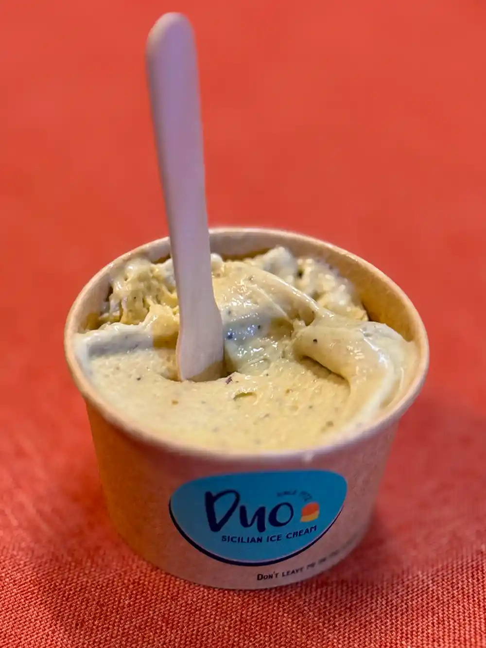 Duo-Gelato-Eiscreme Ein Becher mit sizilianischem Eis mit einem Holzlöffel auf einer roten Fläche.
