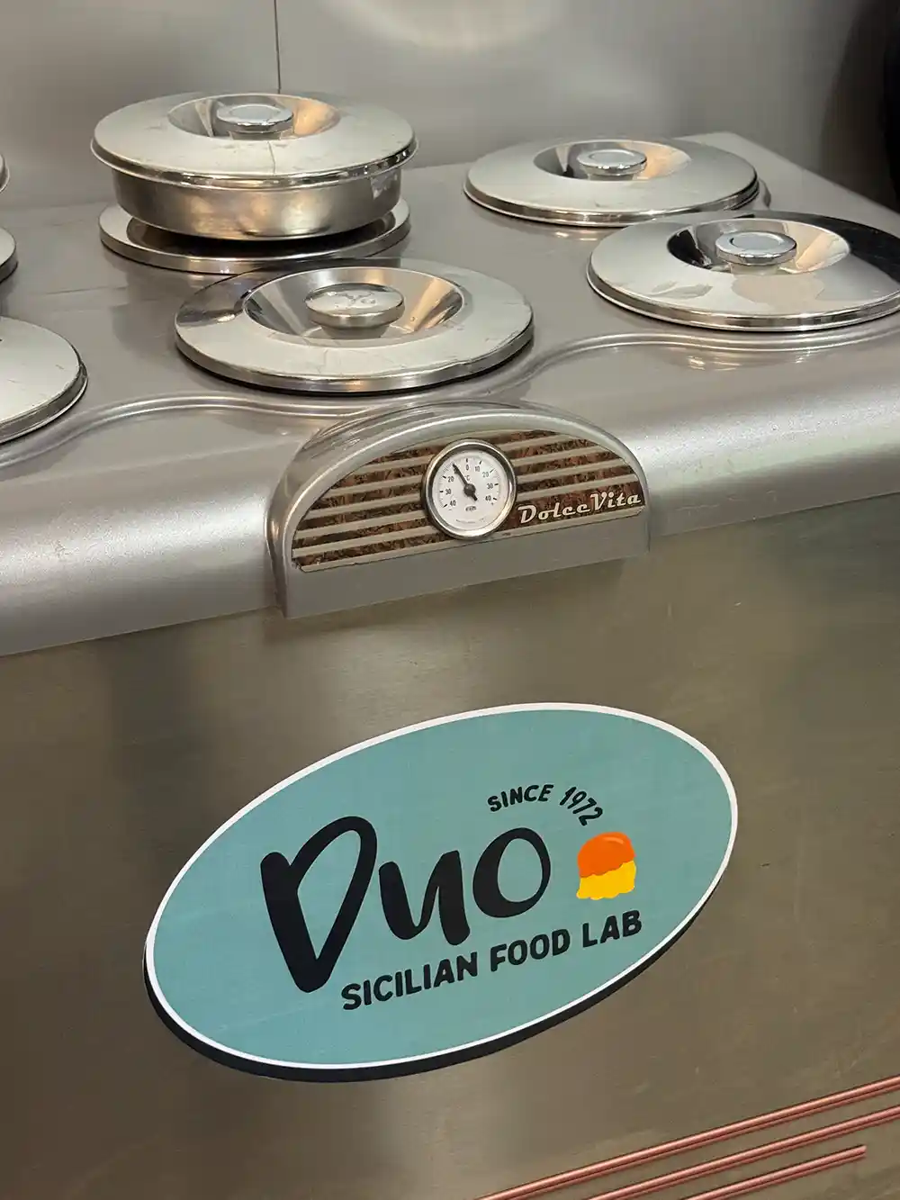Duo-Sicilian-Food-Lab Vier Metalldeckel von Gelatinebehältern auf einer Maschine mit der Aufschrift Dolce Vita und einem Aufkleber des Duo Sicilian Food Lab.
