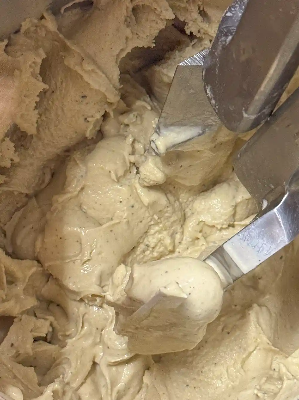 Duo-italienisches-Gelato Dickes, hellbraunes Speiseeis wird mit Metallschaufeln in einer Maschine gemischt.