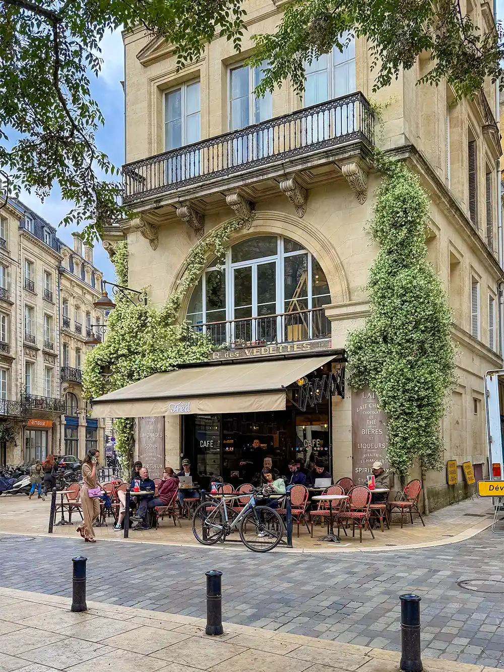 Geheimtipps-Bordeaux-Chez-Fred Außencafé mit roten Stühlen und sitzenden Menschen an einer Straßenecke eines alten, mit Efeu bewachsenen Gebäudes.