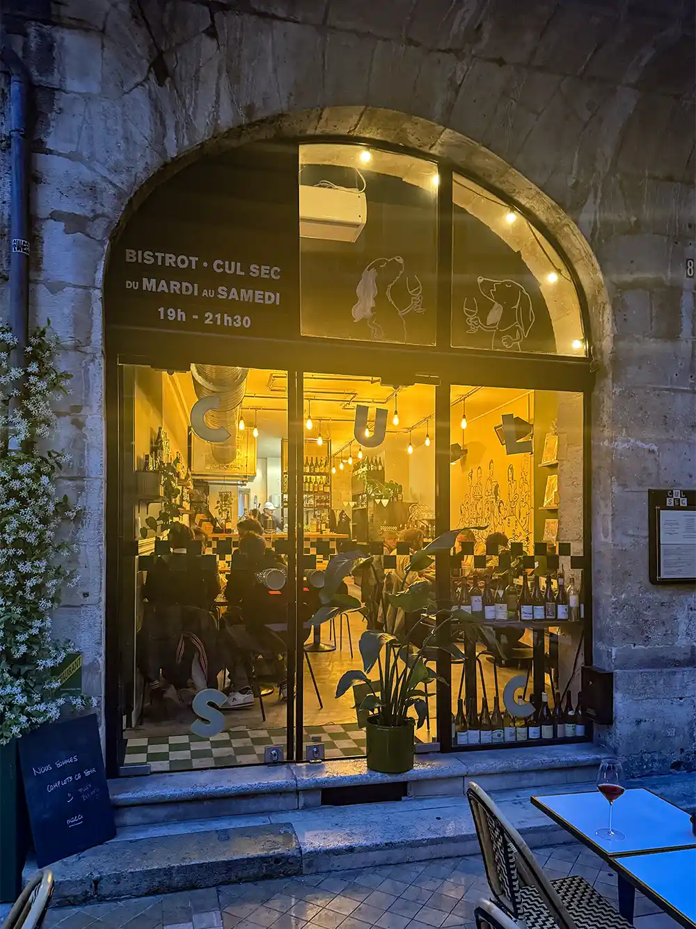 Geheimtipps-Bordeaux-CulSec Ein gemütliches, warm beleuchtetes Bistro, in dem nachts durch große Bogenfenster gegessen wird.