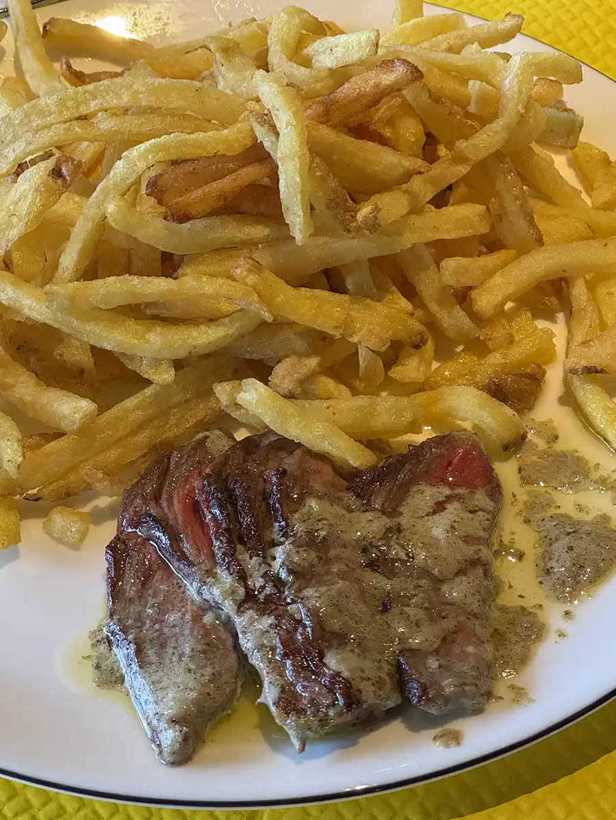 Geheimtipps-Bordeaux-Restaurant-L-Entrecote-Pommes Teller mit Pommes frites und in Scheiben geschnittenem Steak mit Sahnesauce auf einem weißen Teller.