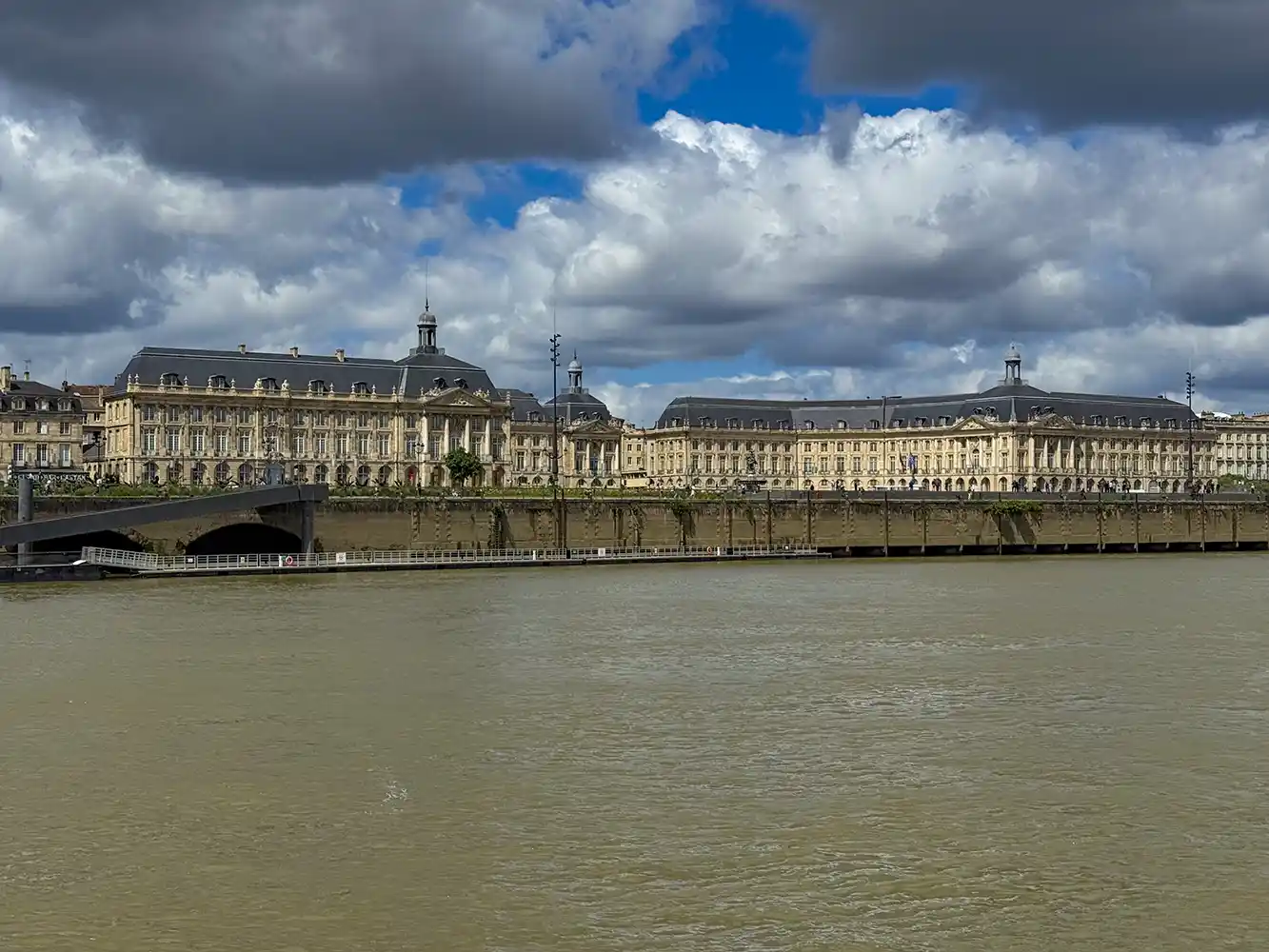 Bordeaux-Geheimtipp-Bootsfahrt Große klassische Gebäude mit Bogenfenstern am Flussufer unter einem teilweise bewölkten Himmel.