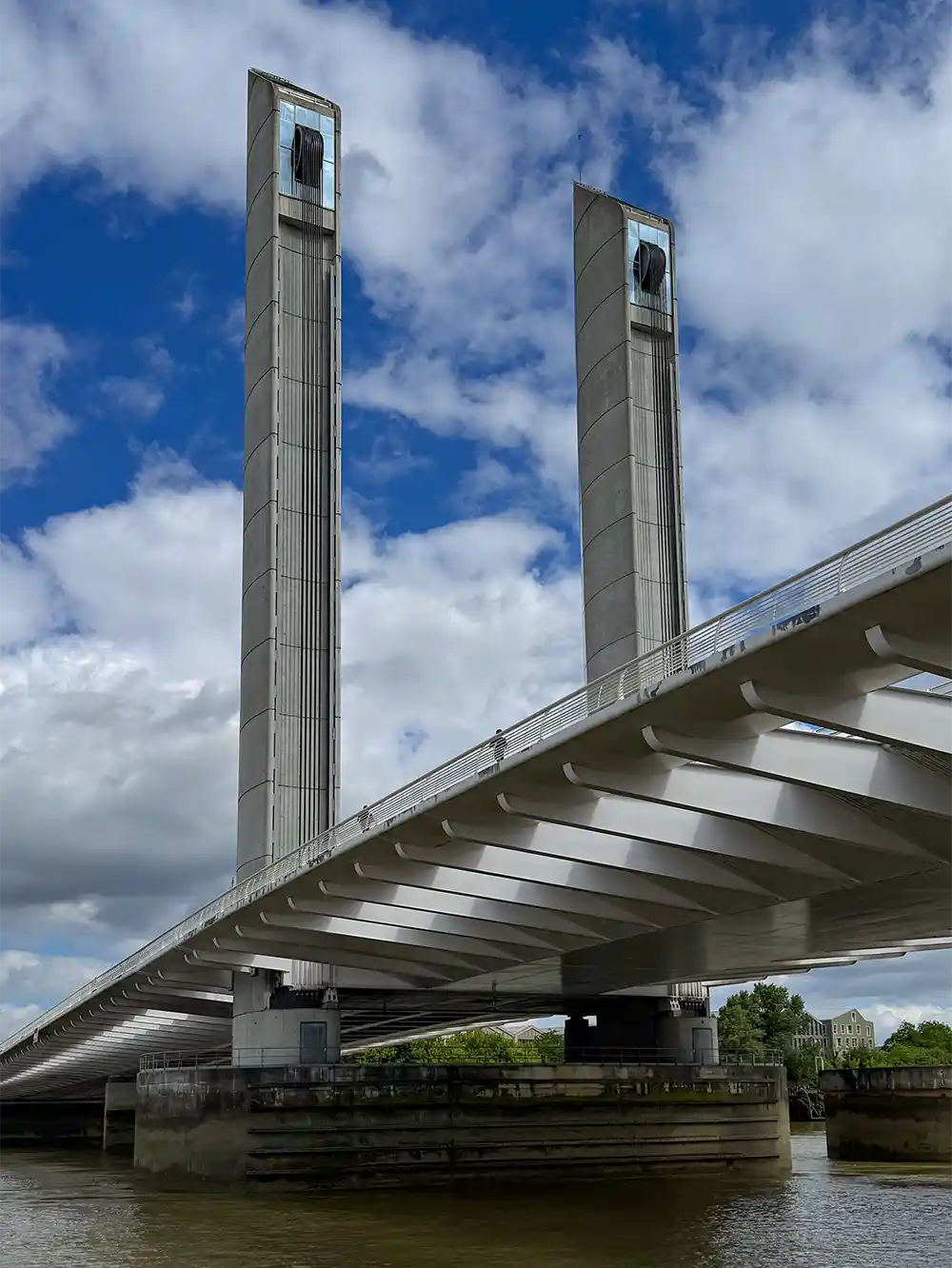 Bordeaux-Geheimtipp-Pont-Jacques-Chaban-Delmas Eine moderne Zugbrücke mit hohen, senkrechten Türmen über einem Fluss unter teilweise bewölktem Himmel.