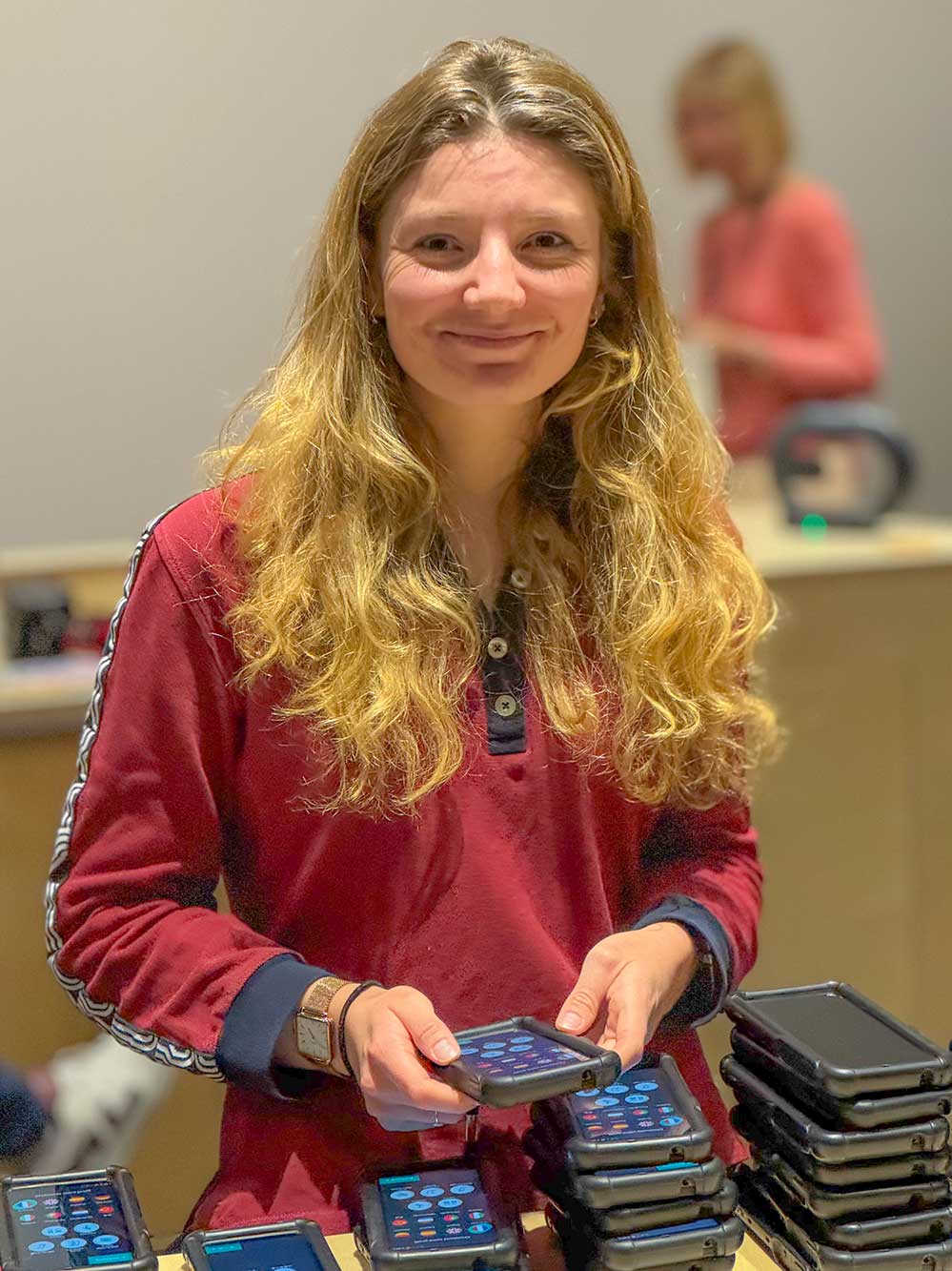 Eine Frau lächelt, während sie einen Audioguide in der Hand hält die aussehen wie Handys.