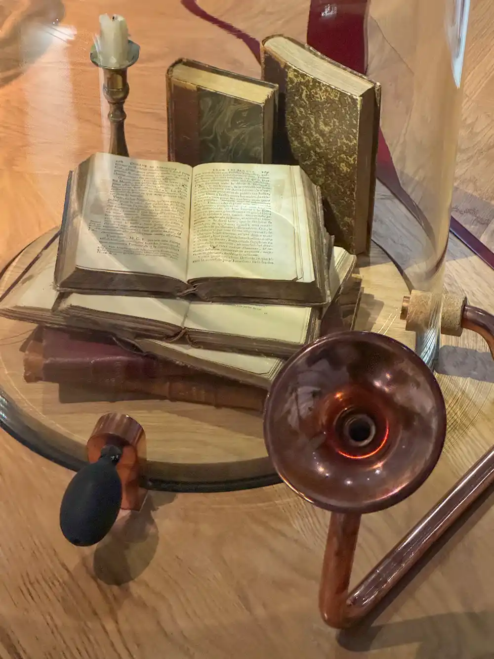 Alte Bücher, ein Kerzenständer und ein altes Hörgerät, ausgestellt auf einem Holztisch unter einer Glasabdeckung.