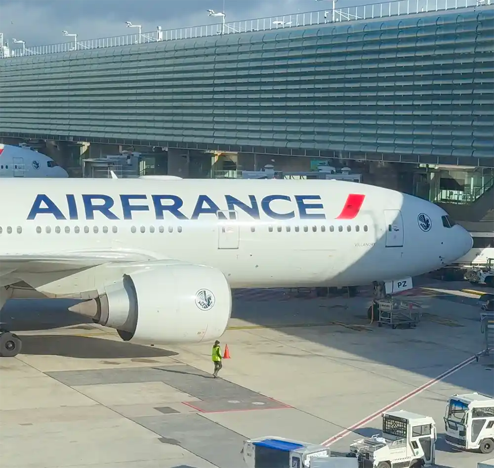 Ein Flugzeug der Air France steht an einem Flugsteig, in dessen Nähe sich Servicefahrzeuge befinden.