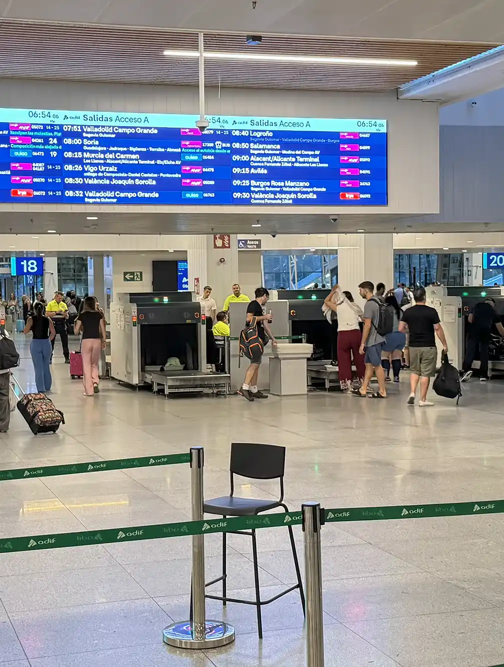 Madrid-Bahnhof-Sicherheitskontrollen Die Menschen passieren die Sicherheitskontrolle an einem Bahnhof, über dem eine große Abfahrtstafel mit den Zugzeiten angebracht ist.