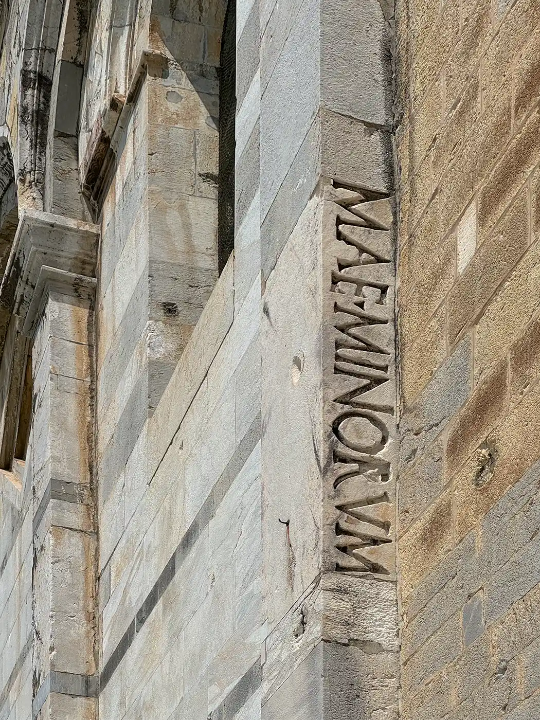 Eine alte Steinmauer, auf deren Ecksäule vertikal das Wort „MAE.Minorum“ eingraviert ist.