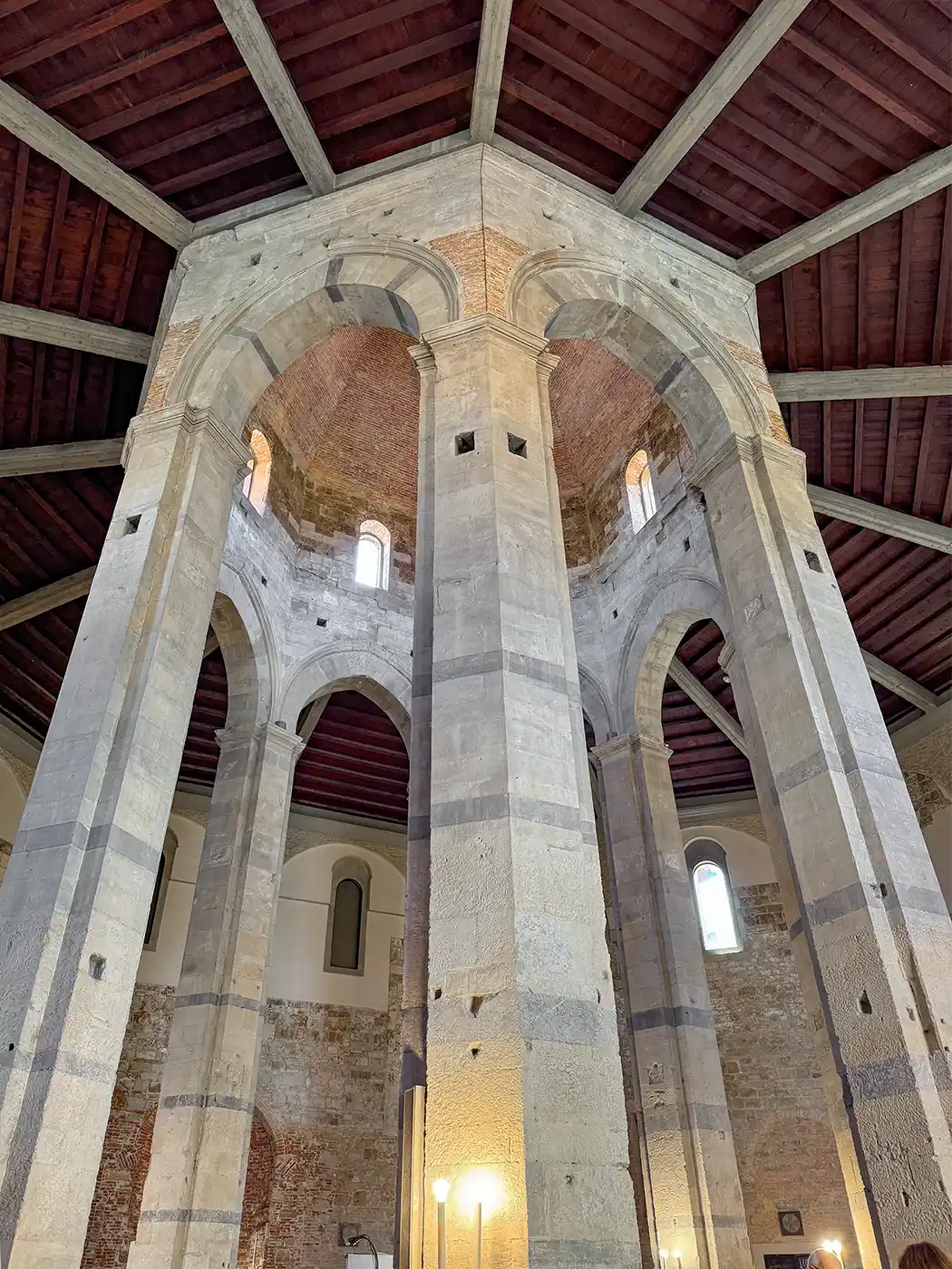 Pisa-Geheimtipp-Chiesa-del-Santo-Sepolcro-innen Innenansicht einer achteckigen Kirchenkuppel aus Stein mit hohen Bögen und hölzernen Deckenpaneelen.