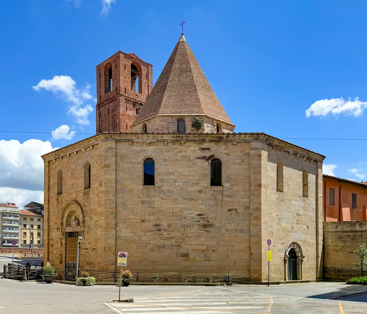 Pisa-Geheimtipp-Chiesa-del-Santo-Sepolcro Steinkirche mit kegelförmigem Dach und Glockenturm vor blauem Himmel mit vereinzelten Wolken.