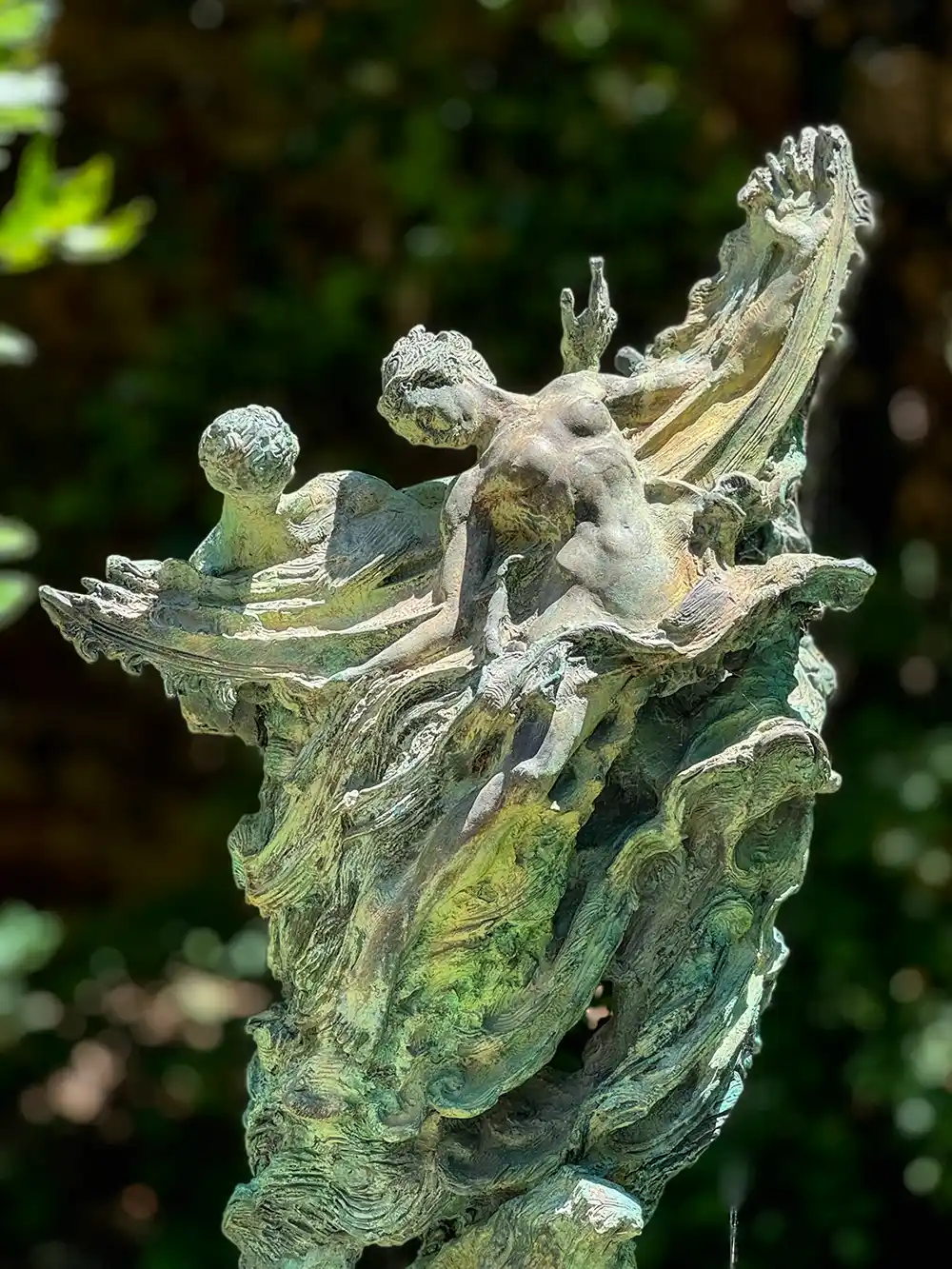 Bronzeskulptur mit abstrakten menschlichen Figuren, die aus wirbelnden, strukturierten Formen im Freien hervortreten, im Hintergrund ist Grün zu sehen.