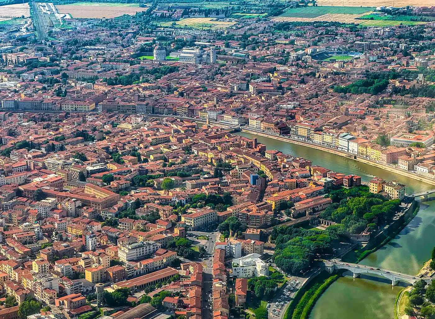 Luftaufnahme einer Stadt mit Gebäuden mit roten Dächern, einem sich schlängelnden Fluss und mehreren grünen Parks.